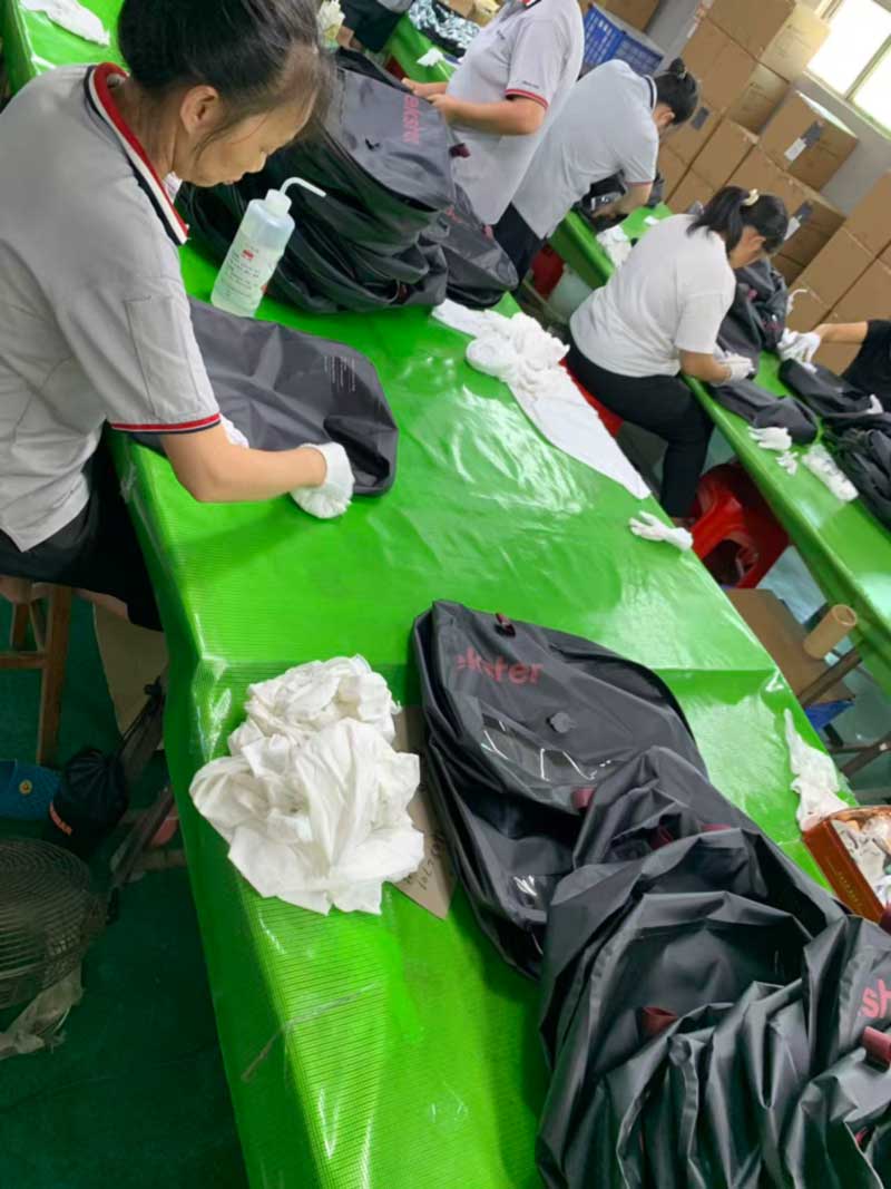 Operators in white gloves wiping down gloss black welded bags at the cleaning bench